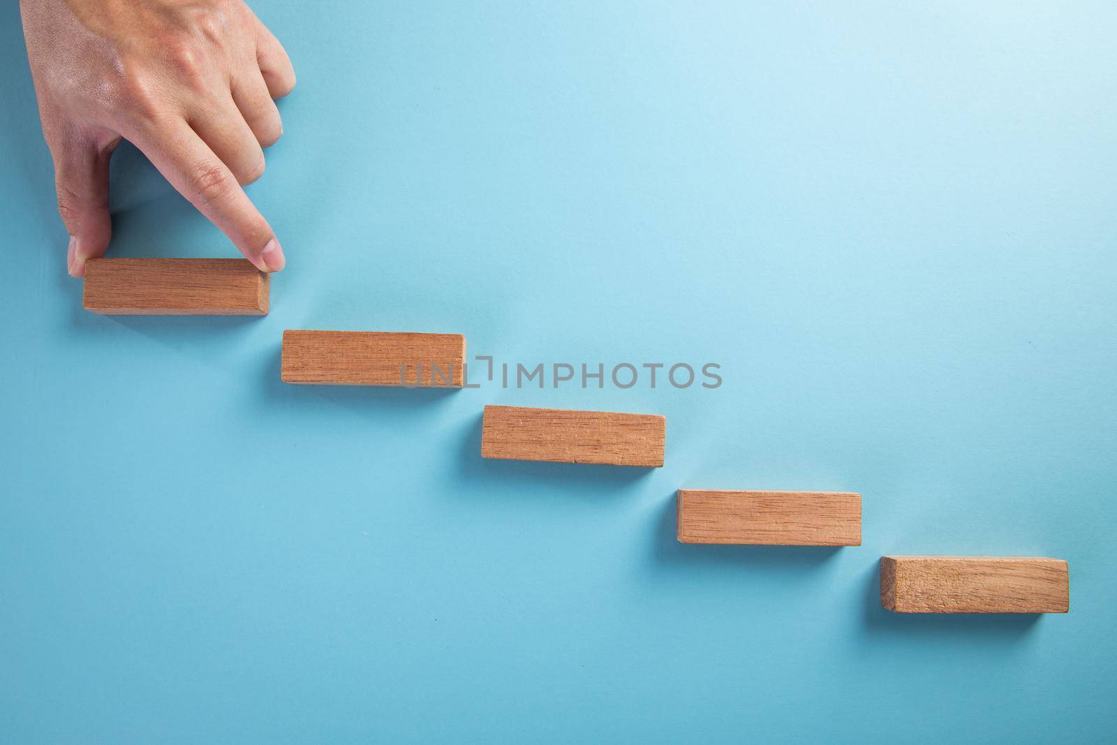 Concept of business development stages. Hand holds wooden block on blue background