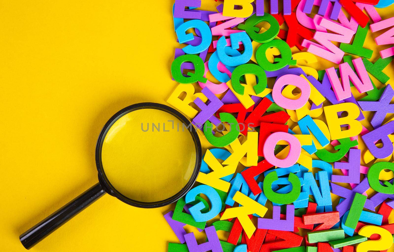 Magnifying glass with colorful alphabet on yellow background.Education concept.