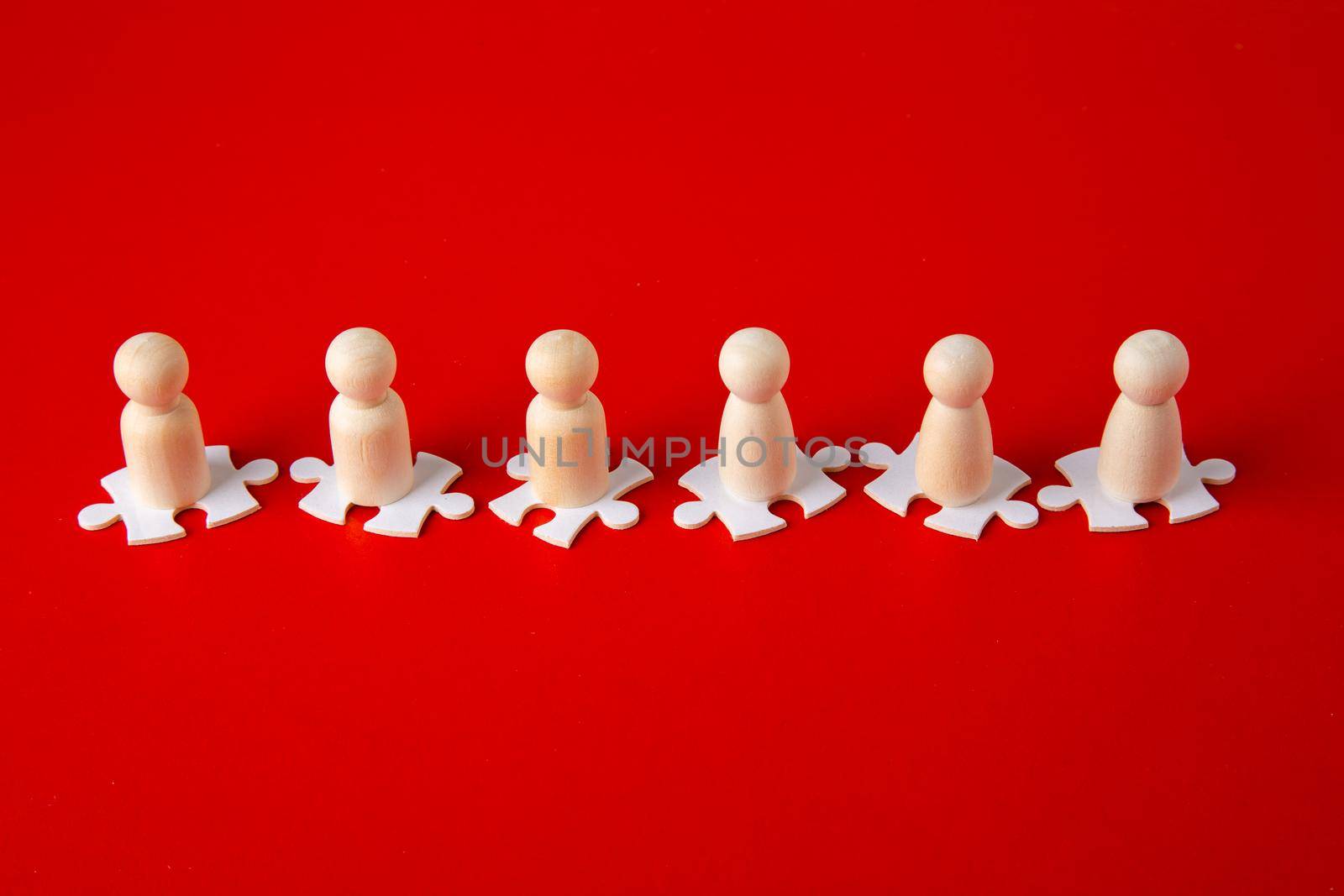 Wooden figures on puzzles on red background as a symbol of team building. Organization group people in business. Cooperation and partnership.