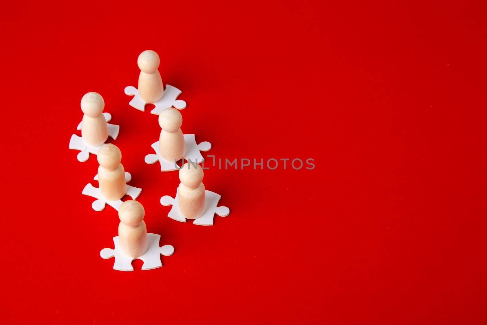 Wooden figures on puzzles on red background as a symbol of team building. Organization group people in business. Cooperation and partnership.