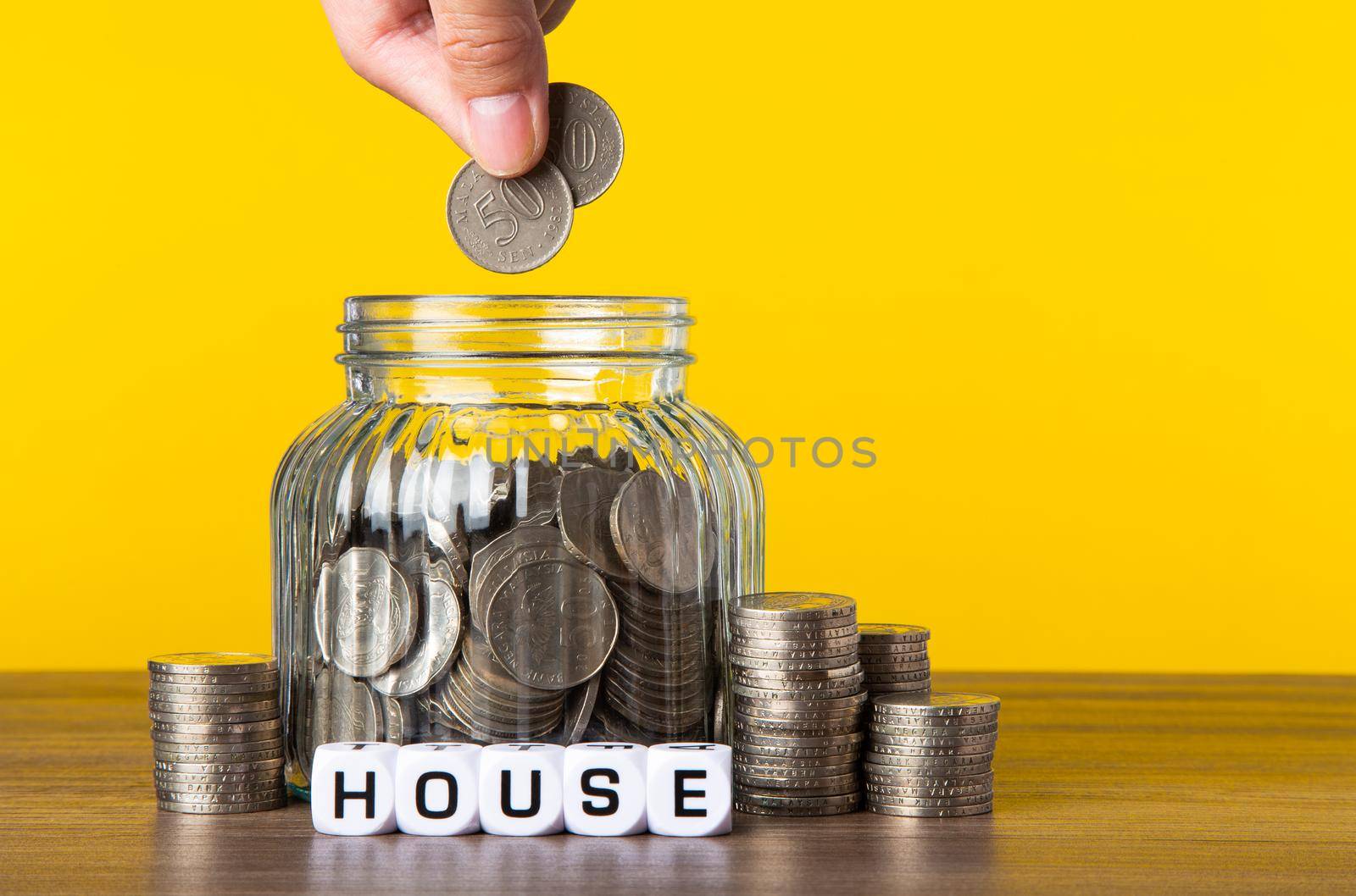 A lot coins in glass money jar with yellow background. Saving for House concept.