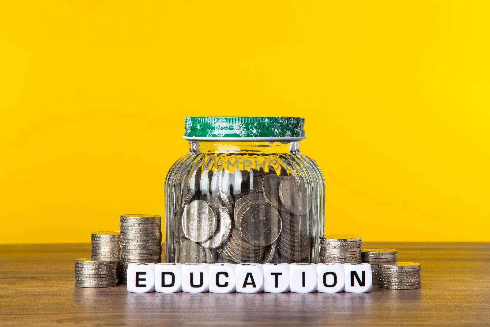 A lot coins in glass money jar with yellow background. Saving for Education concept.
