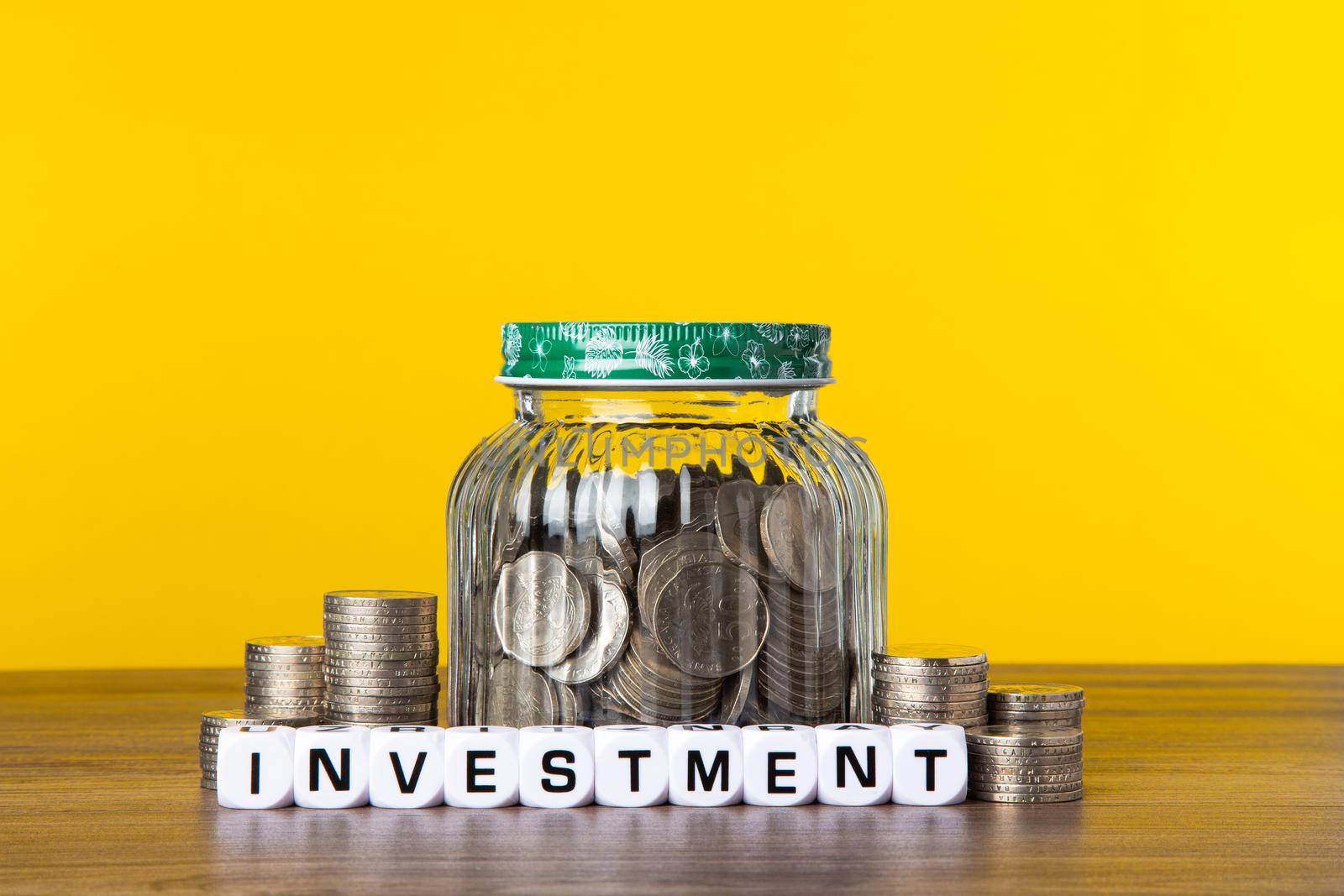 A lot coins in glass money jar with yellow background. Saving for Investment concept.