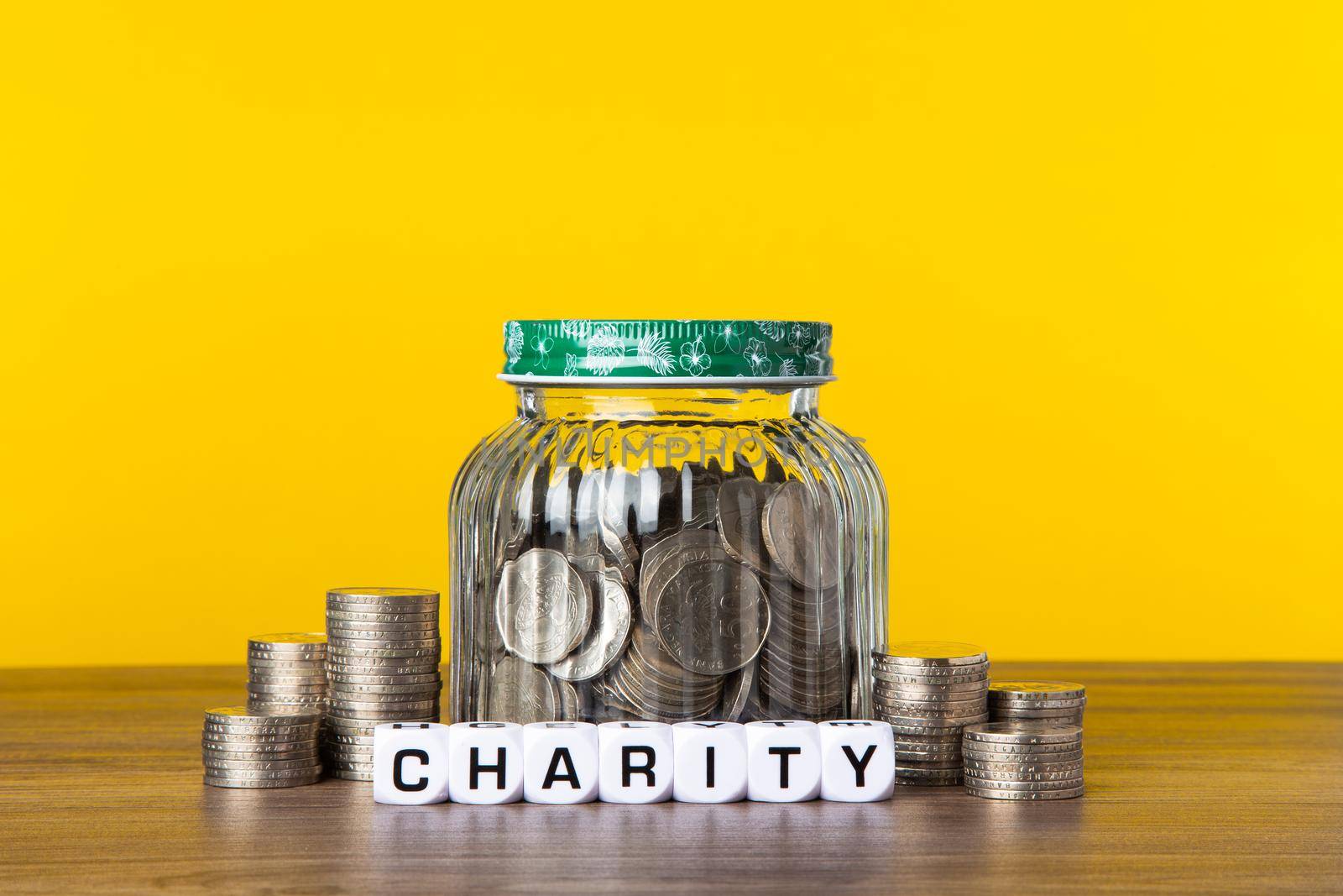 A lot coins in glass money jar with yellow background. Saving for Charity concept.
