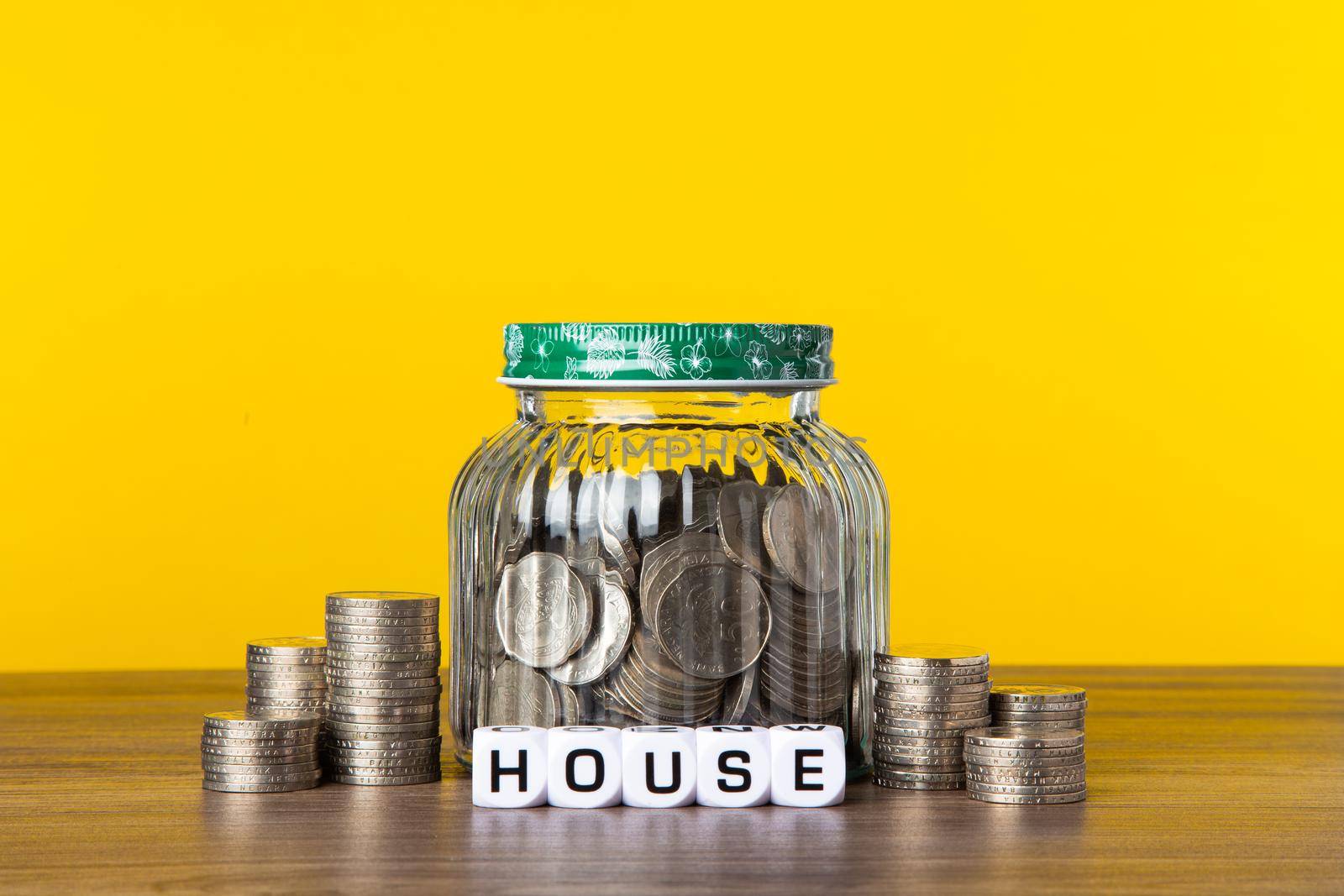 A lot coins in glass money jar with yellow background. Saving for House concept.