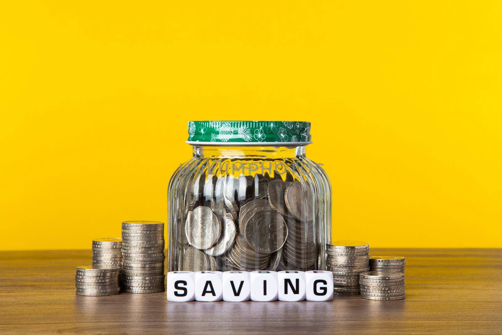 A lot coins in glass money jar with yellow background. Saving for Investment concept.