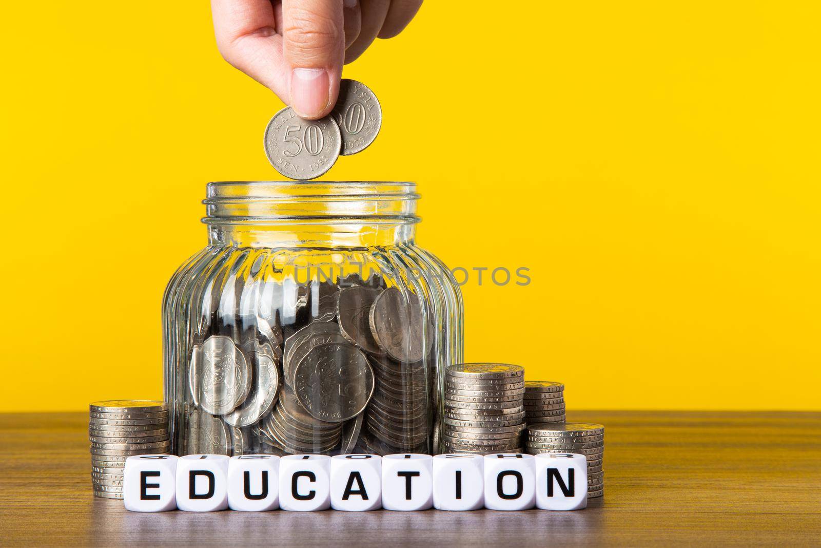 A lot coins in glass money jar with yellow background. Saving for Education concept.