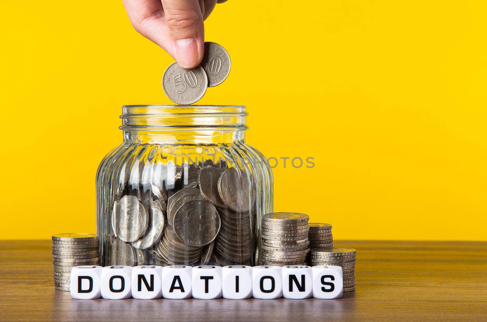 A lot coins in glass money jar with yellow background. Saving for Donations concept.