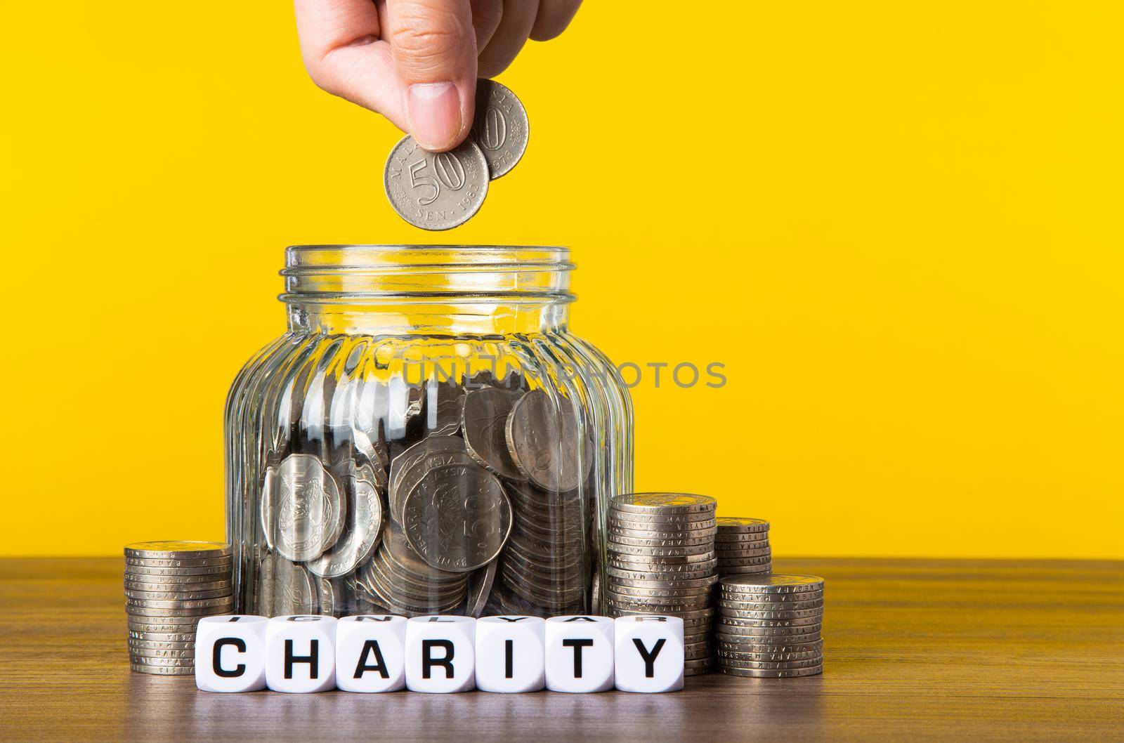 A lot coins in glass money jar with yellow background. Saving for Charity concept.
