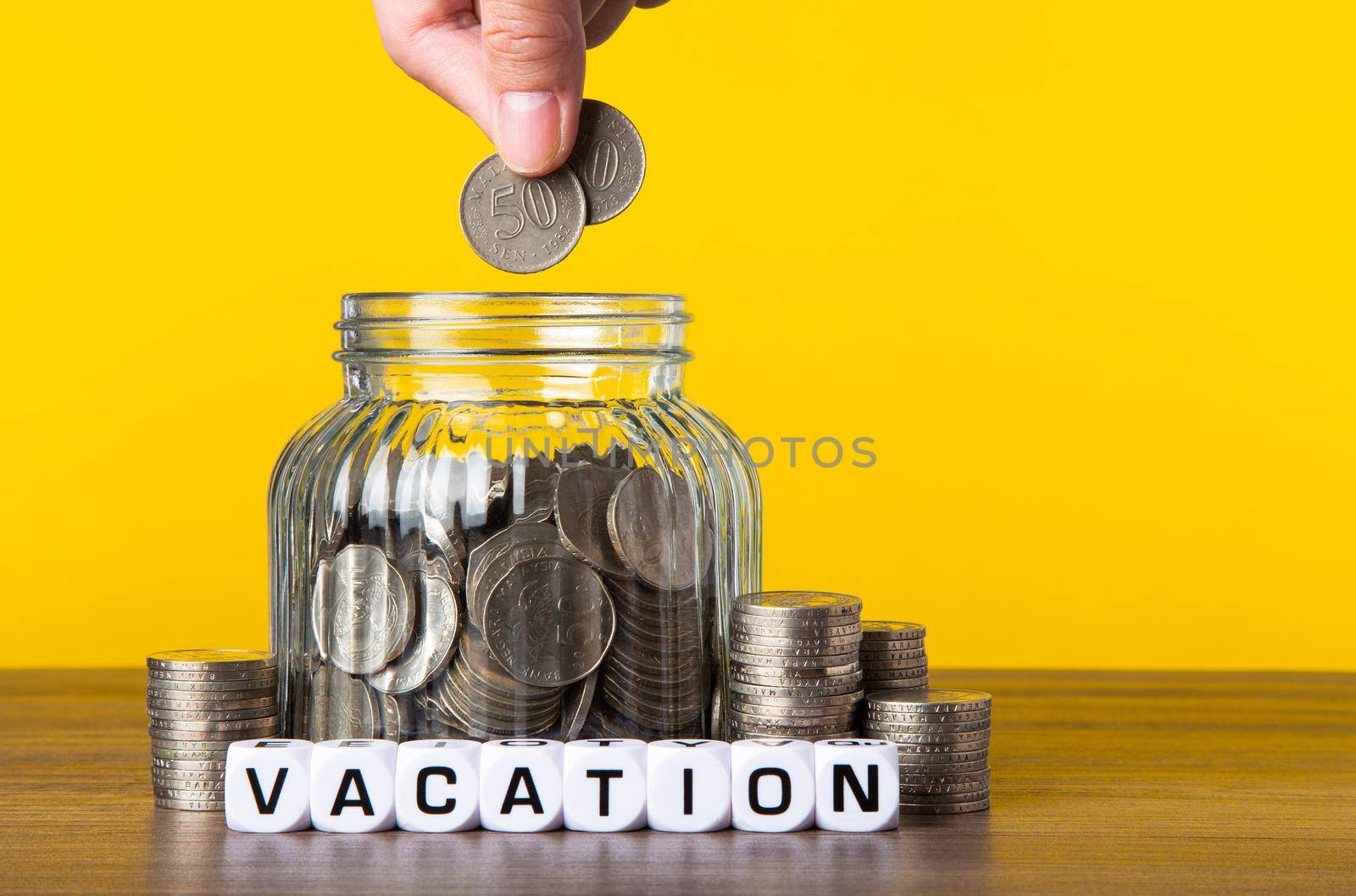 A lot coins in glass money jar with yellow background. Saving for Vacation concept.