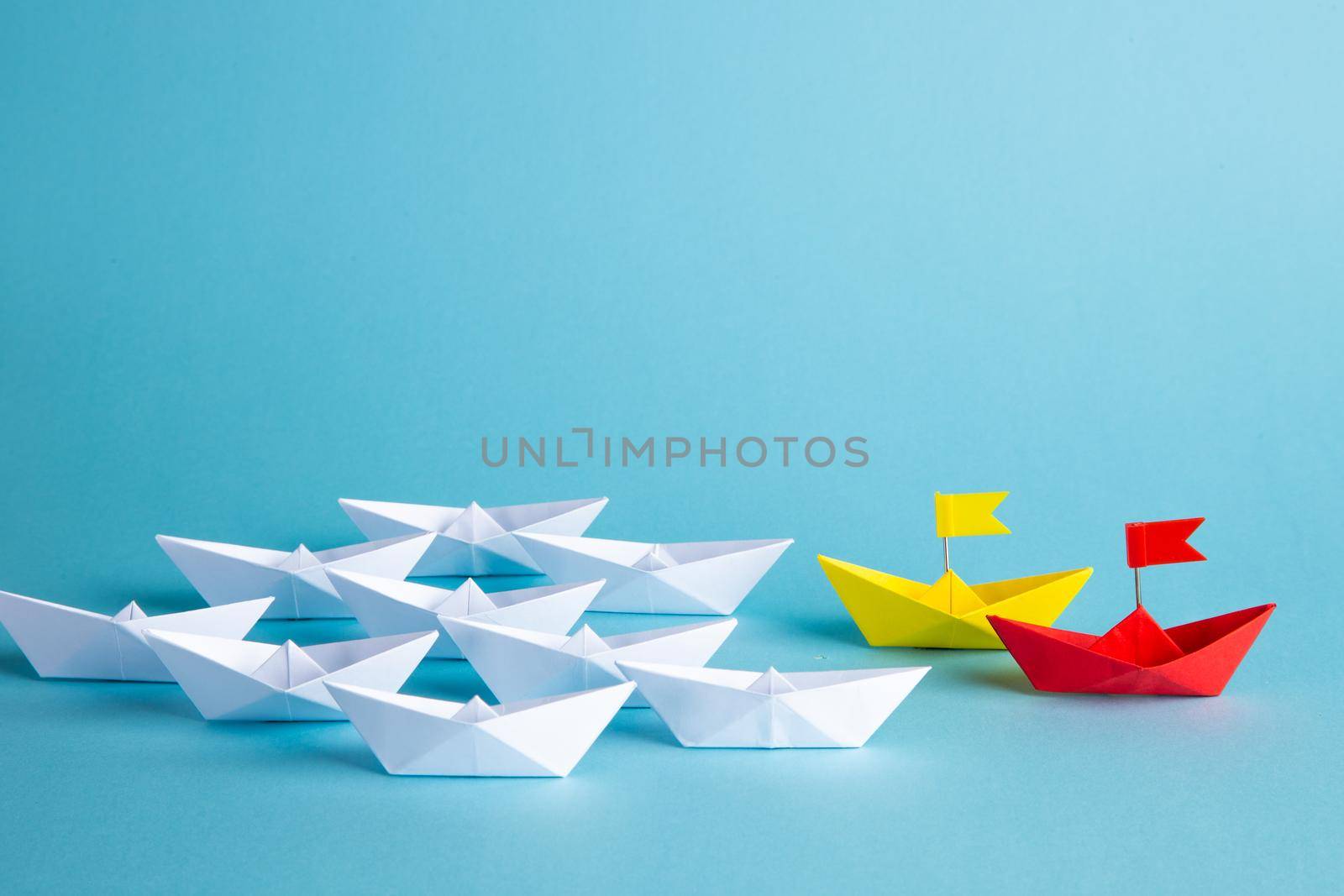 Leadership concept. Red leader paper ship leading among others on blue background.