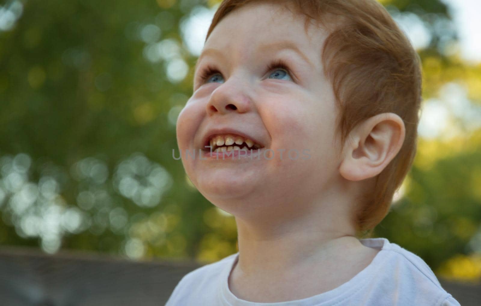 Portrait of a cute, redhead, blue-eyed boy wearing a white t-shirt in a playground on a sunny day