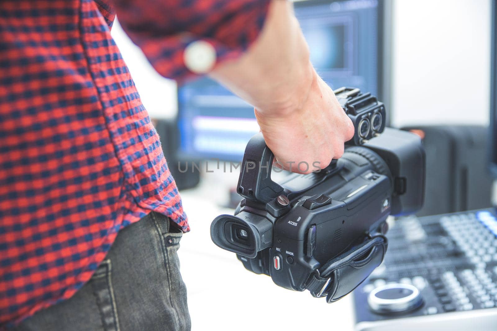 Male cameraman is holding a professional video camcorder, blurry background