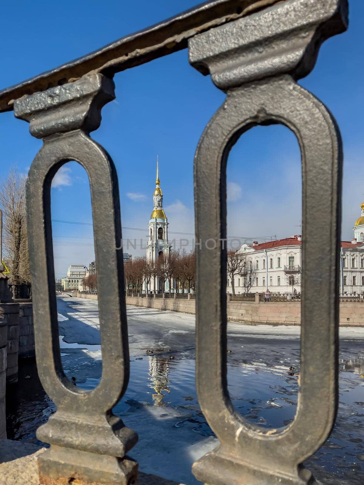 St. Nicholas Naval Cathedral belltower through the forged lattice in a clear sunny day of spring, an ice drift on Kryukov and Griboyedov Canal, a view of seven bridges from the embankment by vladimirdrozdin