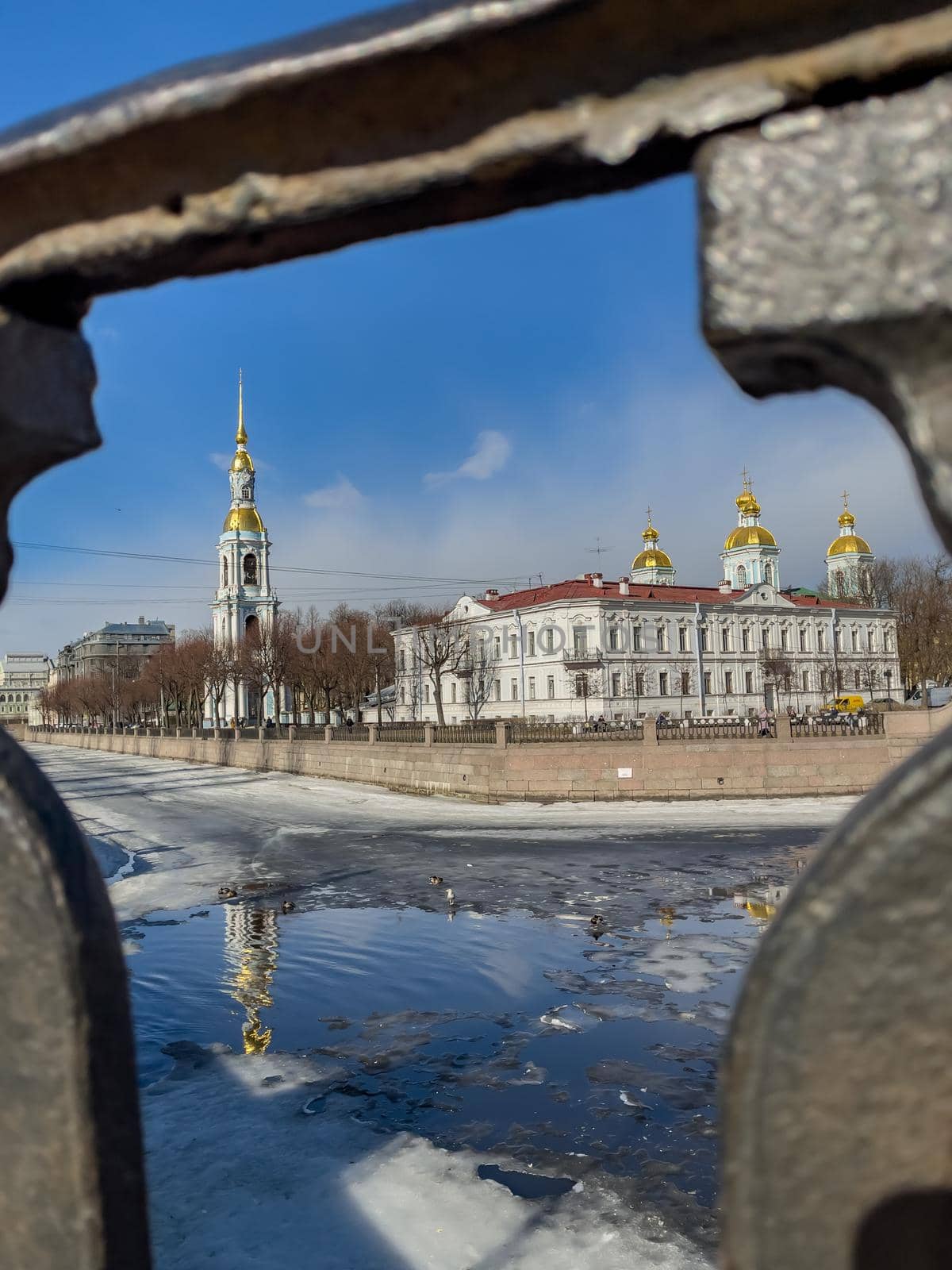 St. Nicholas Naval Cathedral belltower through the forged lattice in a clear sunny day of spring, an ice drift on Kryukov and Griboyedov Canal, a view of seven bridges from the embankment. High quality photo