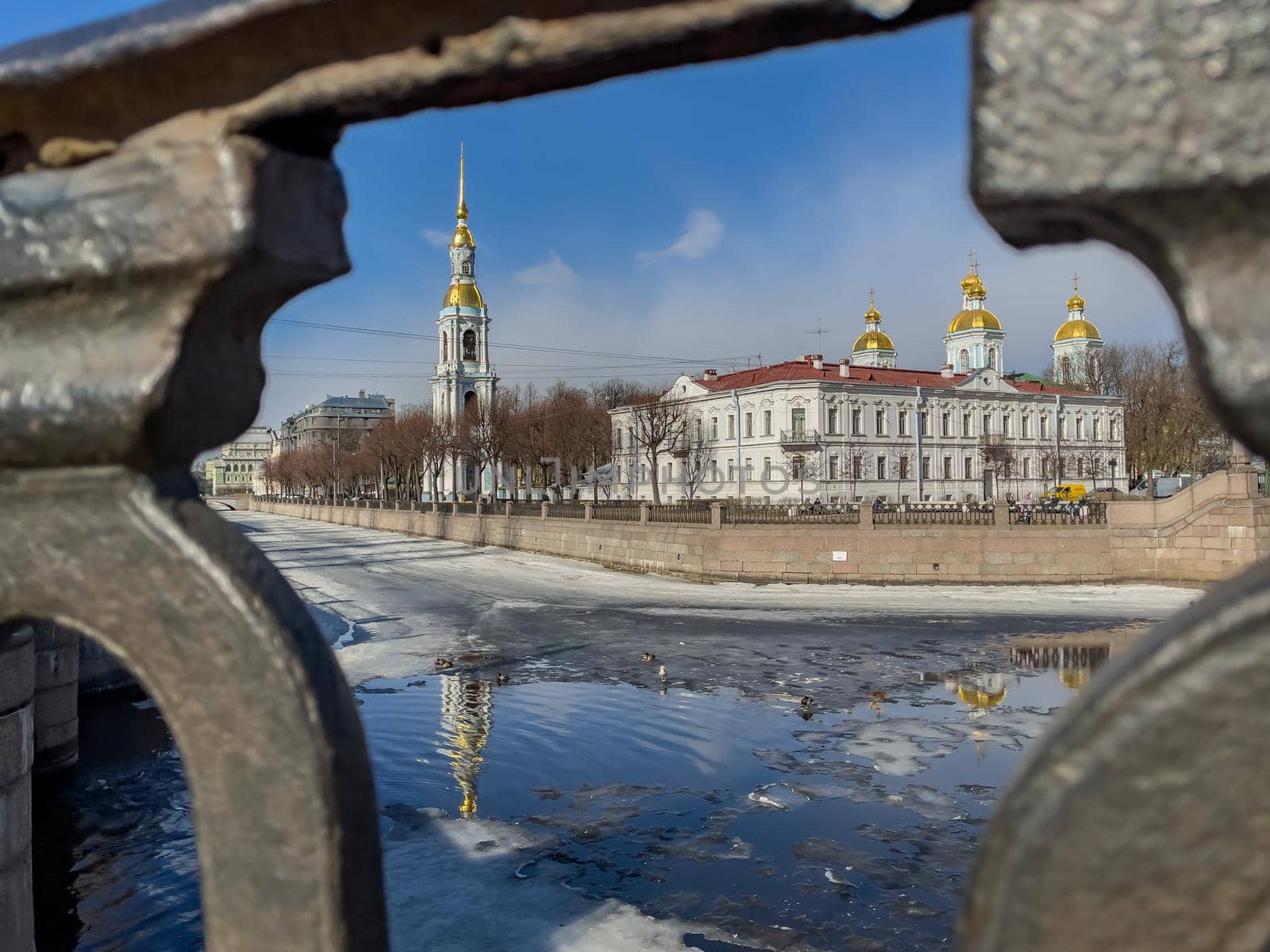 St. Nicholas Naval Cathedral belltower through the forged lattice in a clear sunny day of spring, an ice drift on Kryukov and Griboyedov Canal, a view of seven bridges from the embankment. High quality photo