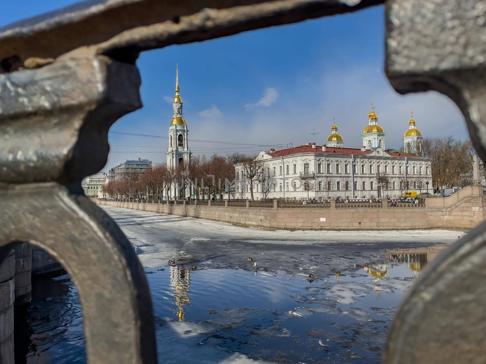 St. Nicholas Naval Cathedral belltower through the forged lattice in a clear sunny day of spring, an ice drift on Kryukov and Griboyedov Canal, a view of seven bridges from the embankment by vladimirdrozdin