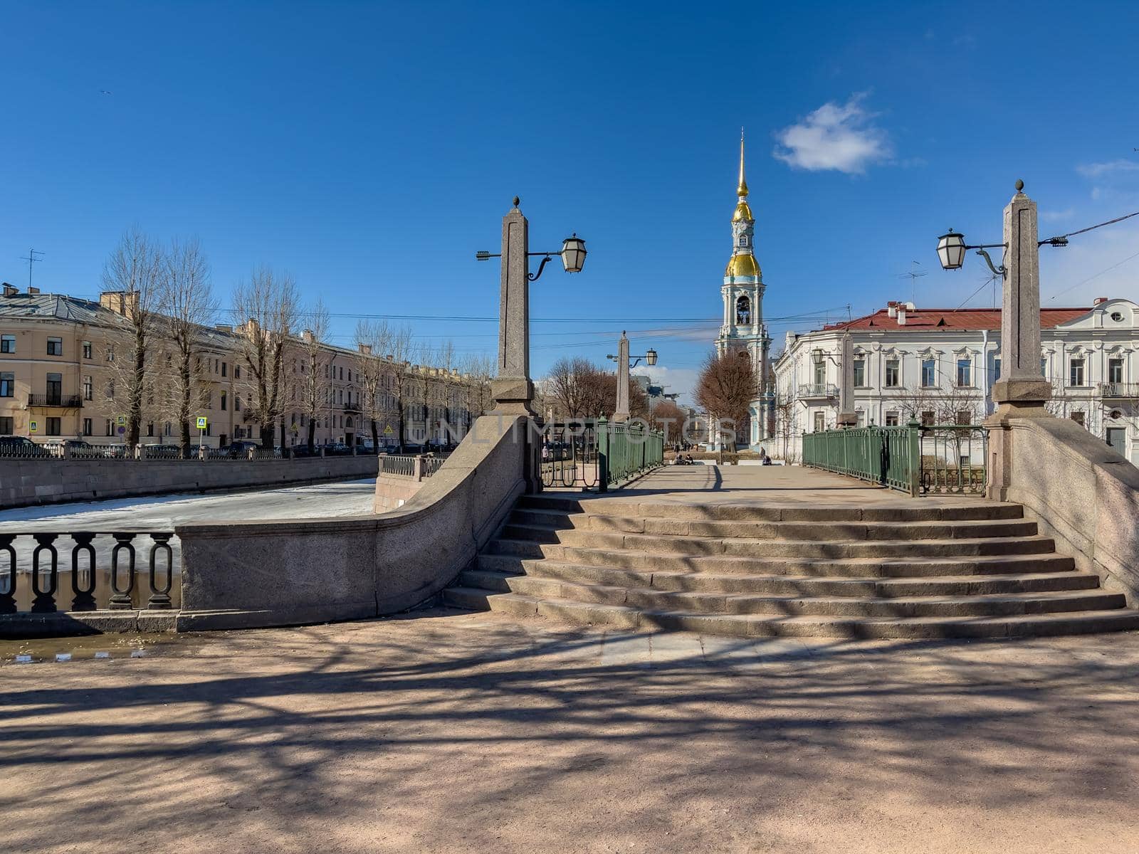 Russia, St. Petersburg, 01 April 2021: St. Nicholas Naval Cathedral belltower in a clear sunny day of spring, an ice drift on Kryukov and Griboyedov Canal, a view of seven bridges from the embankment. High quality photo