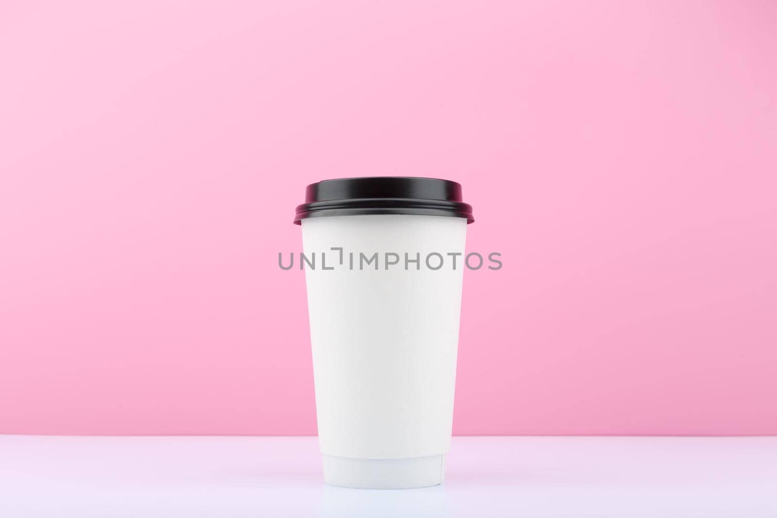 White tall disposable cup for tea or coffee on white table against bright purple background with copy space. Concept of disposable cups and hot drinks