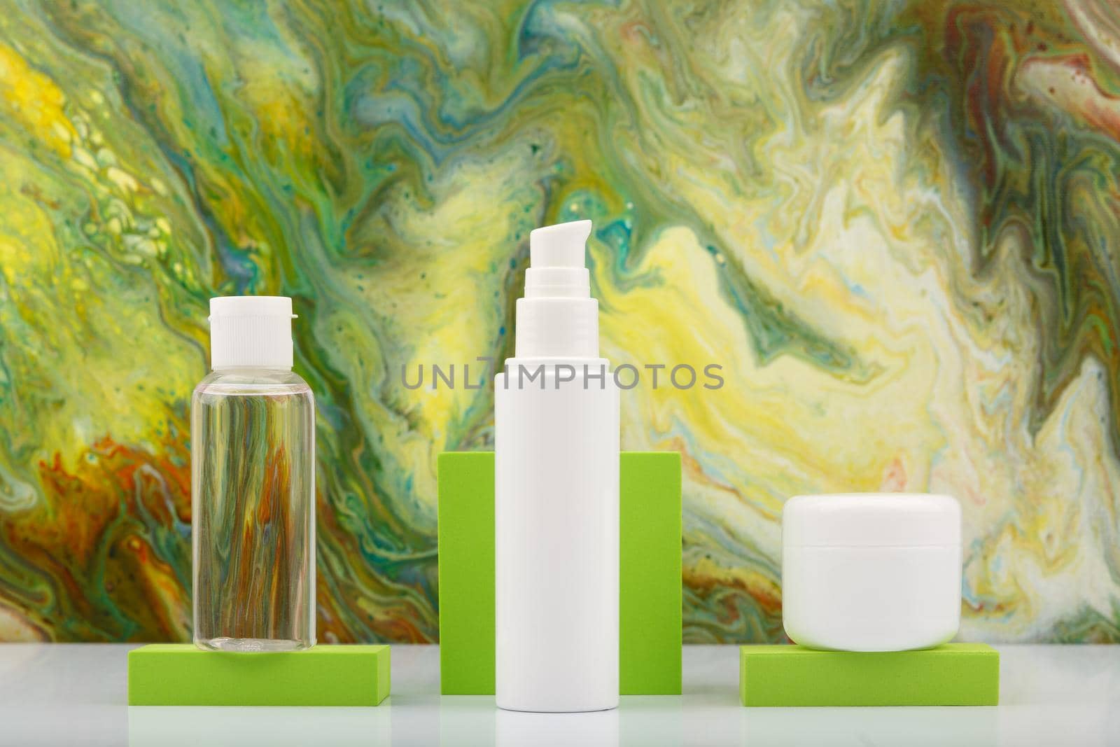 Skin lotion in transparent bottle, face cream and lip balm on green podiums against marbled background in green colors.  by Senorina_Irina