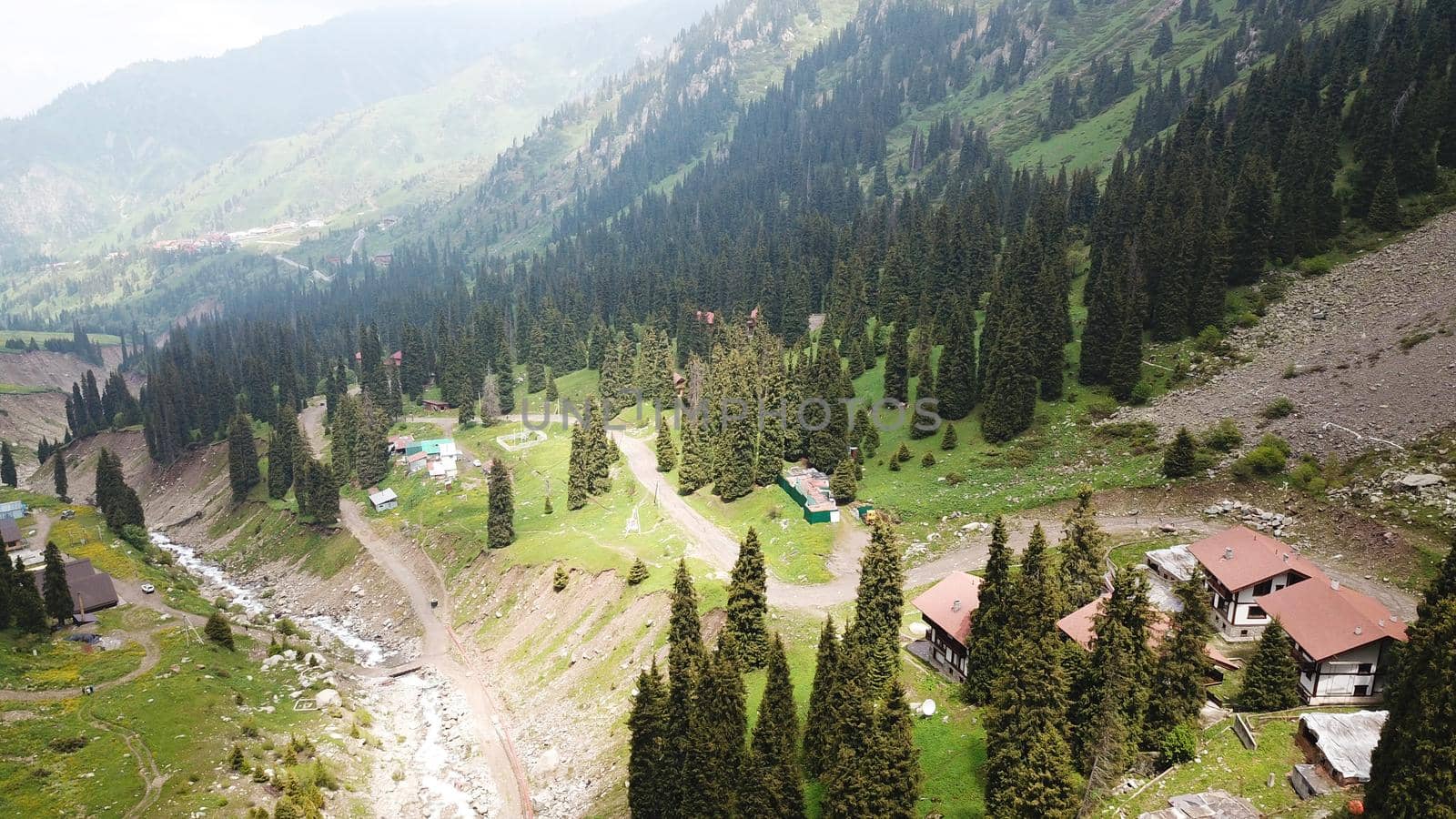 Green gorge with forest in the mountains. Aerial view of green hills, coniferous trees, road, river and trail. Steep cliffs with large rocks. The gorge is foggy, dripping rain in places. Kazakhstan.