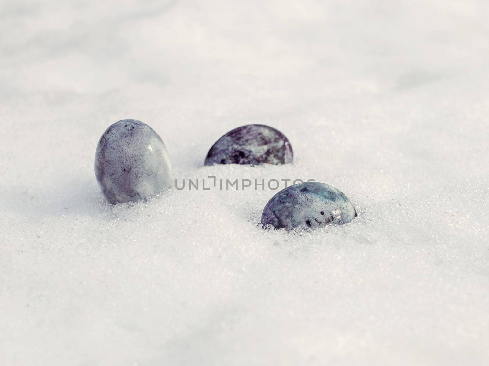 Painted chicken eggs on white snow on spring day.