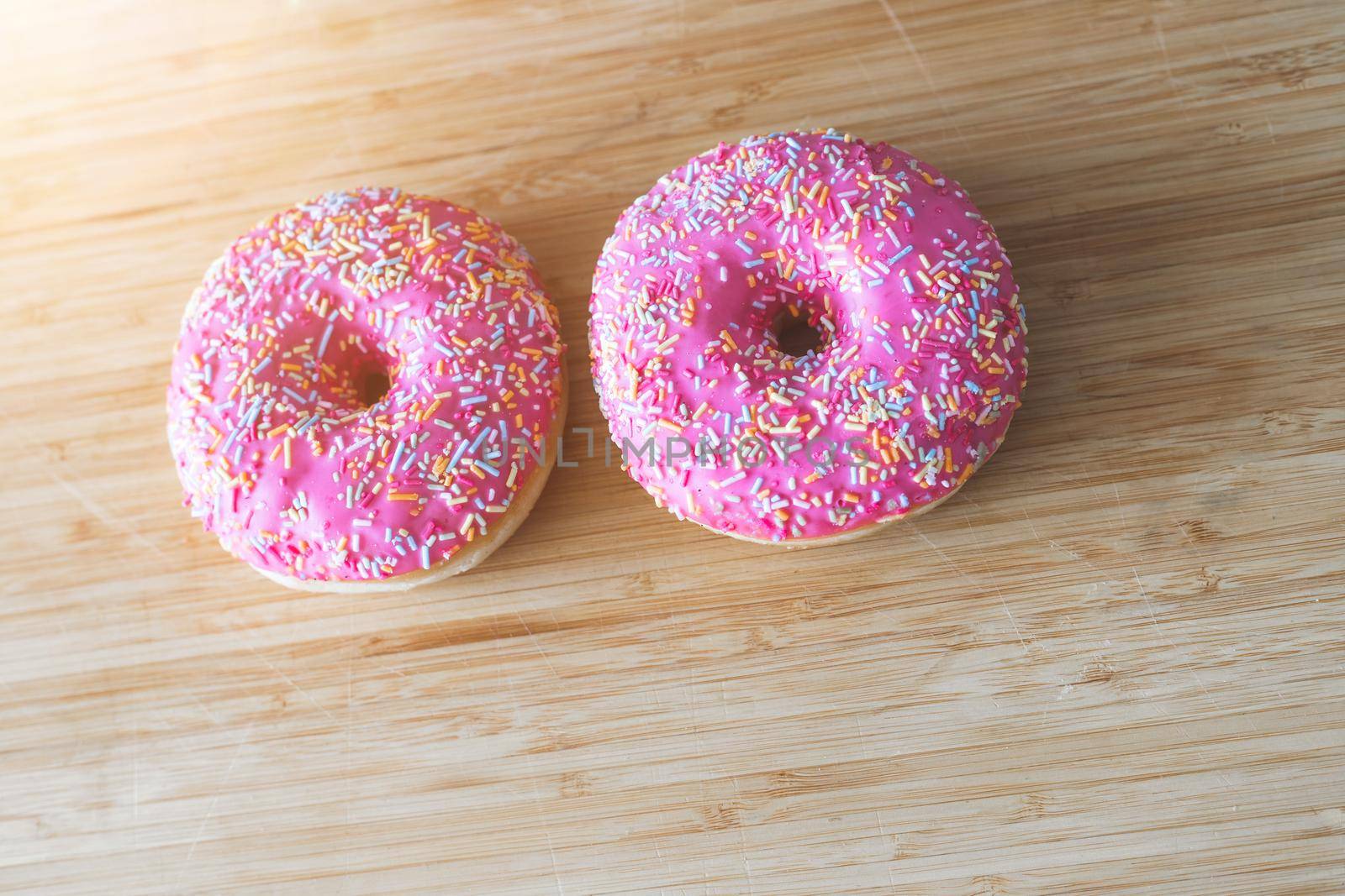 Sugar sprinkled pink donut on wooden plate