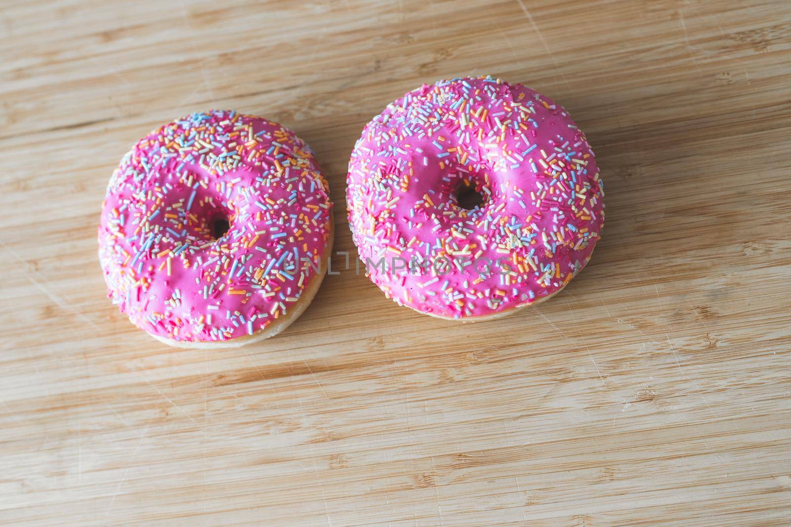 Sugar sprinkled pink donut on wooden plate