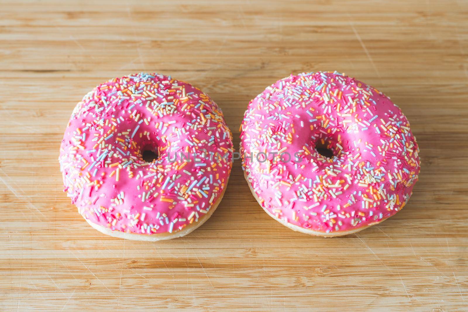 Sugar sprinkled pink donut on wooden plate
