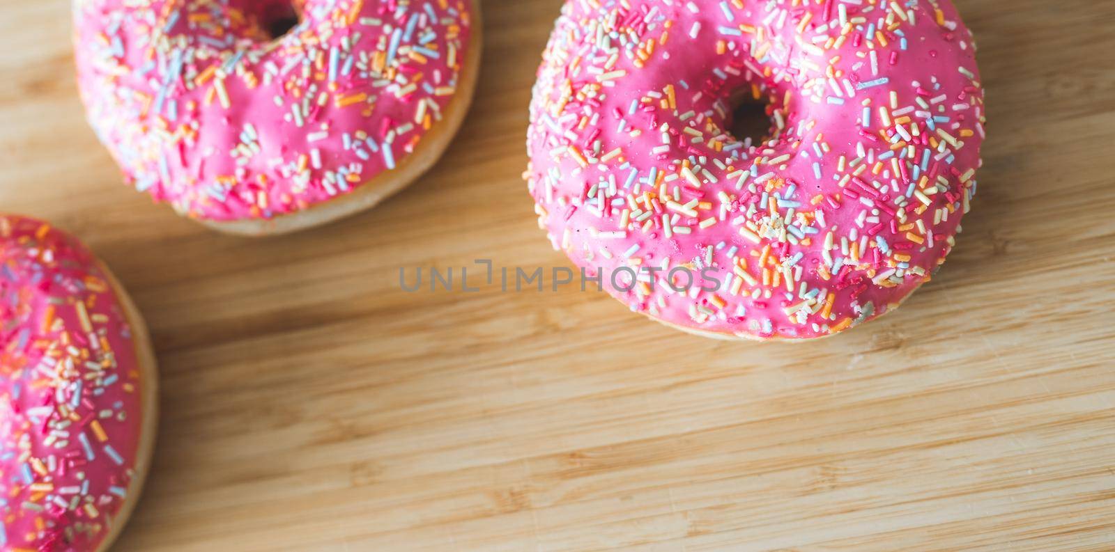 Sugar sprinkled pink donut on wooden plate