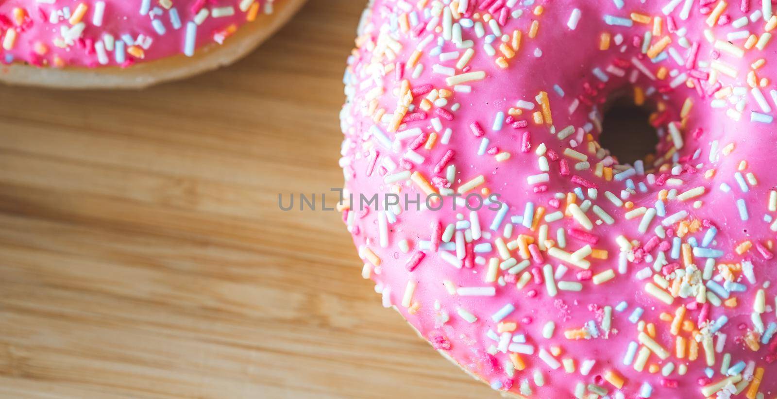 Sugar sprinkled pink donut on wooden plate