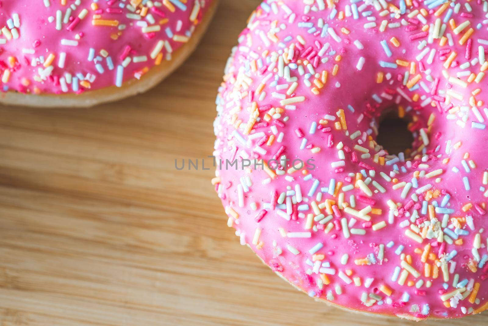 Sugar sprinkled pink donut on wooden plate