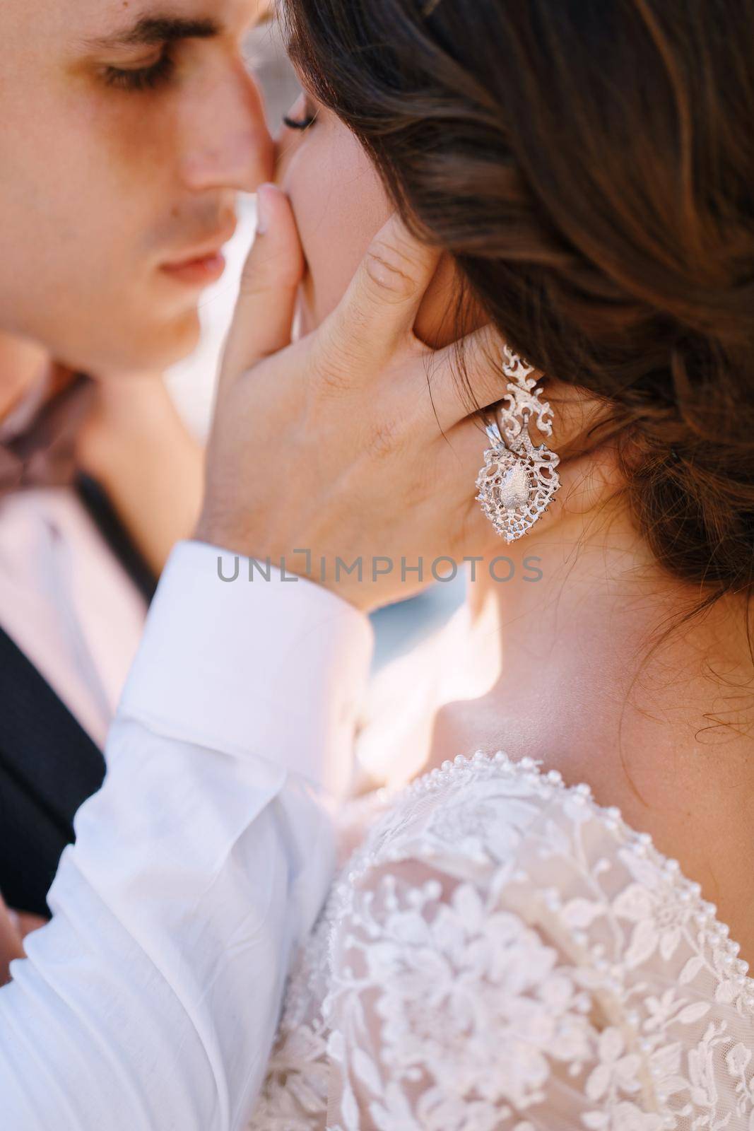 Close-up, the wedding couple is almost kissing. The groom strokes the bride's hand on the cheek. Fine-art wedding photo in Montenegro, Perast. by Nadtochiy