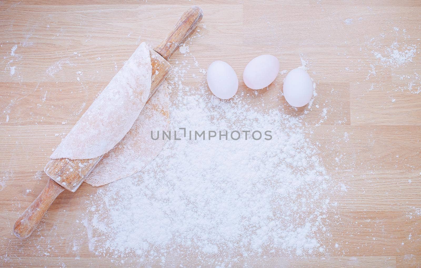 Preparation of dough for Italian pasta from flour and eggs with rolling pin on wooden panel.