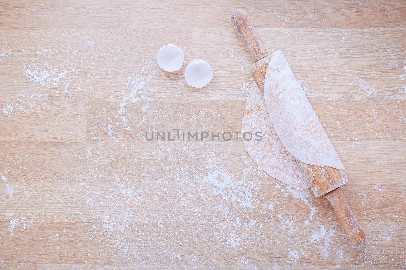 Preparation of dough for Italian pasta from flour and eggs with rolling pin on wooden panel.