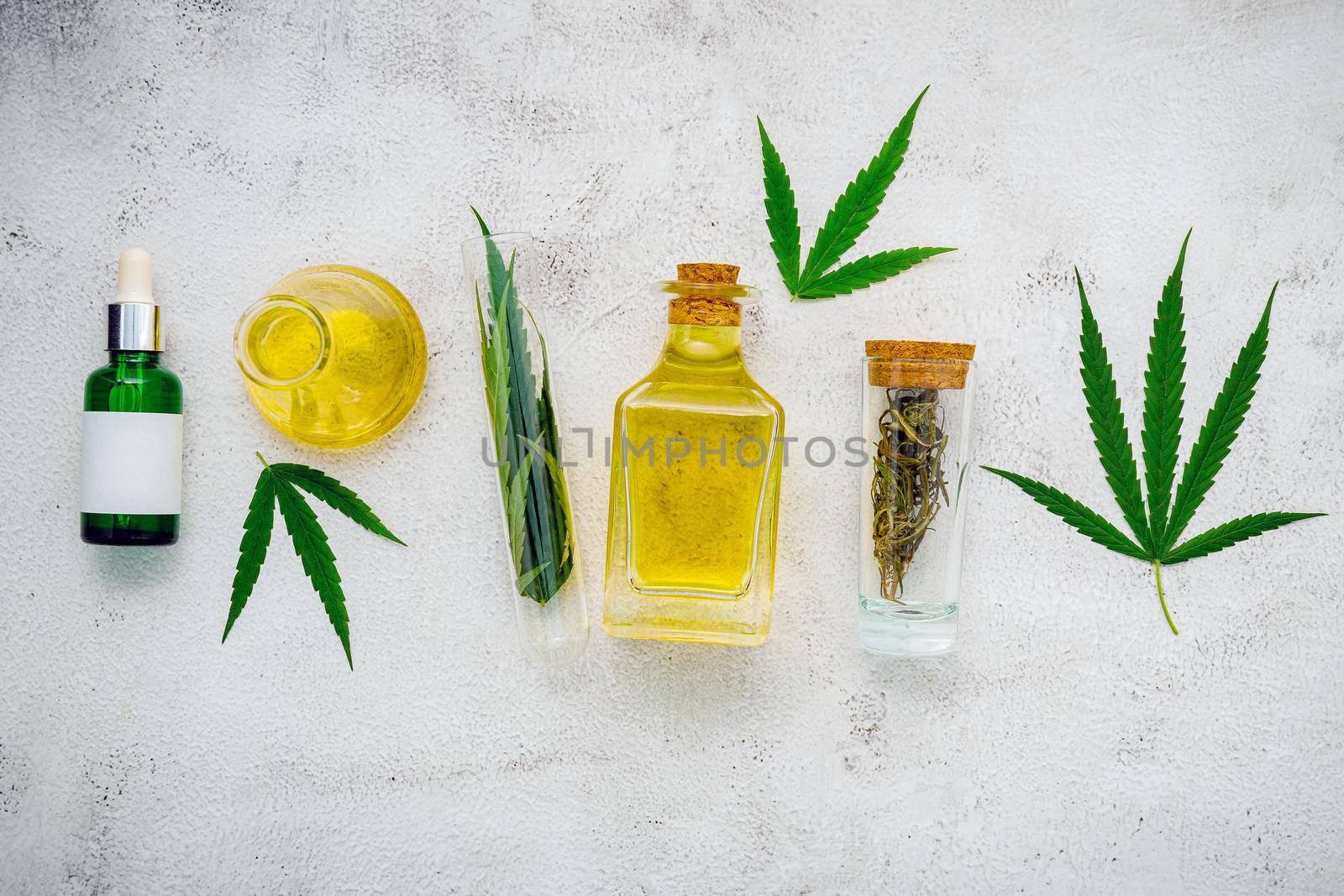 Glass bottle of cannabis oil and hemp leaves set up  on concrete background.