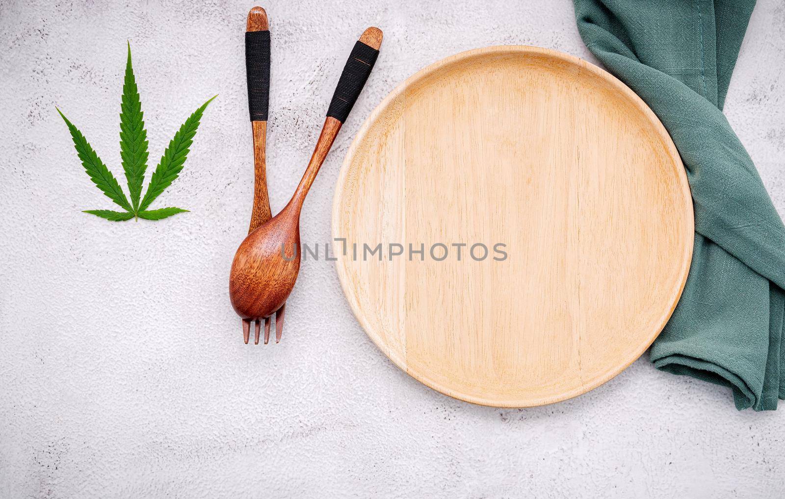 Food conceptual image of a cannabis leaf  with spoon and fork on white concrete background. by kerdkanno