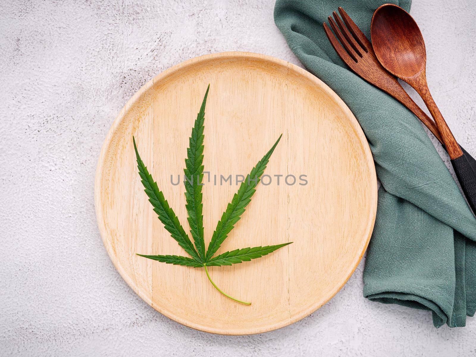 Food conceptual image of a cannabis leaf  with spoon and fork on white concrete background. by kerdkanno