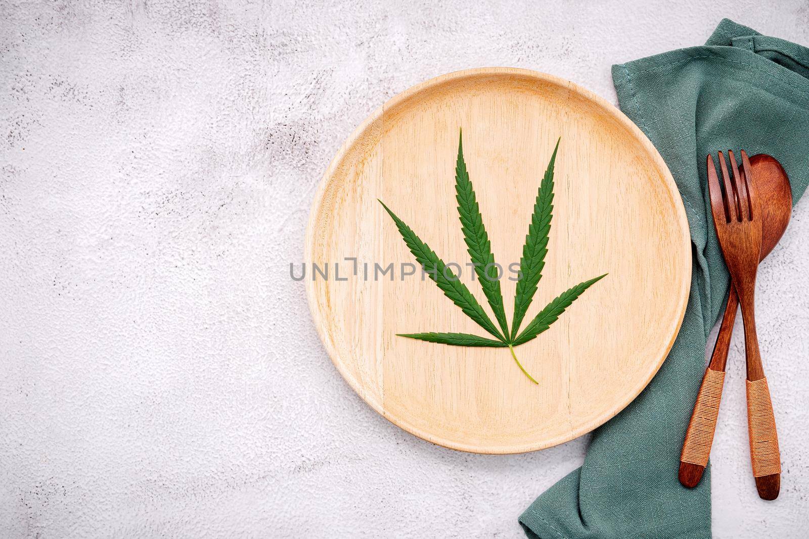 Food conceptual image of a cannabis leaf  with spoon and fork on white concrete background.