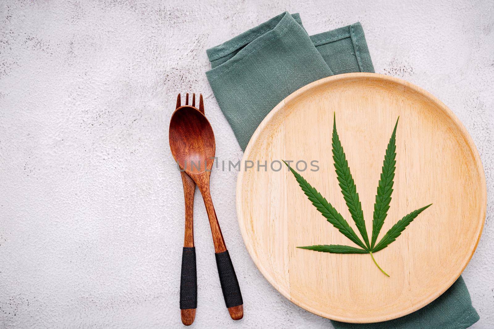 Food conceptual image of a cannabis leaf  with spoon and fork on white concrete background.