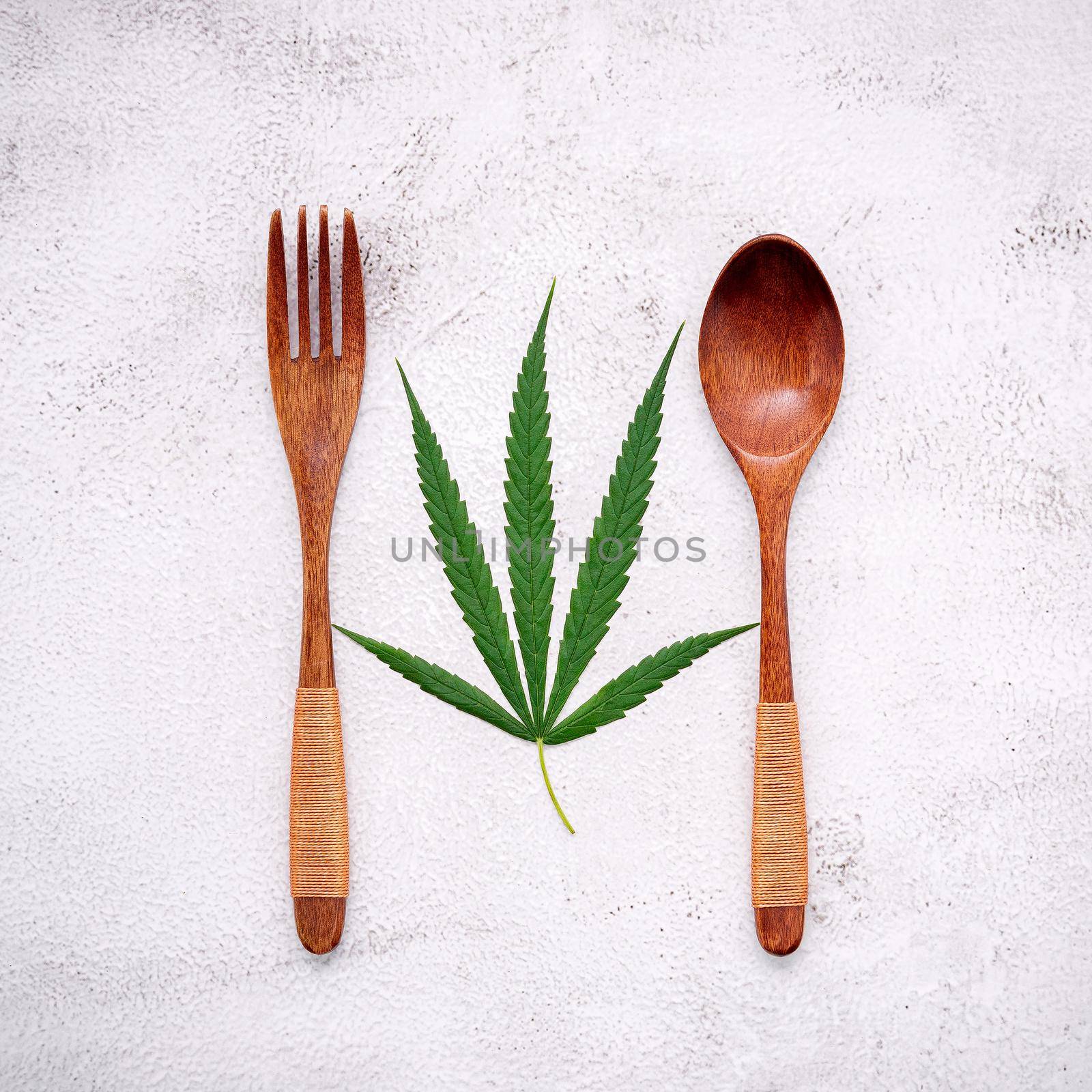 Food conceptual image of a cannabis leaf  with spoon and fork on white concrete background.