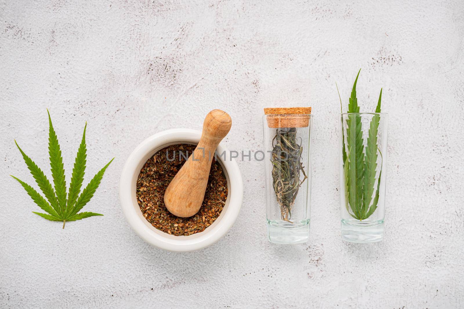 Glass bottle of cannabis oil with white mortar and hemp leaves set up  on concrete background.