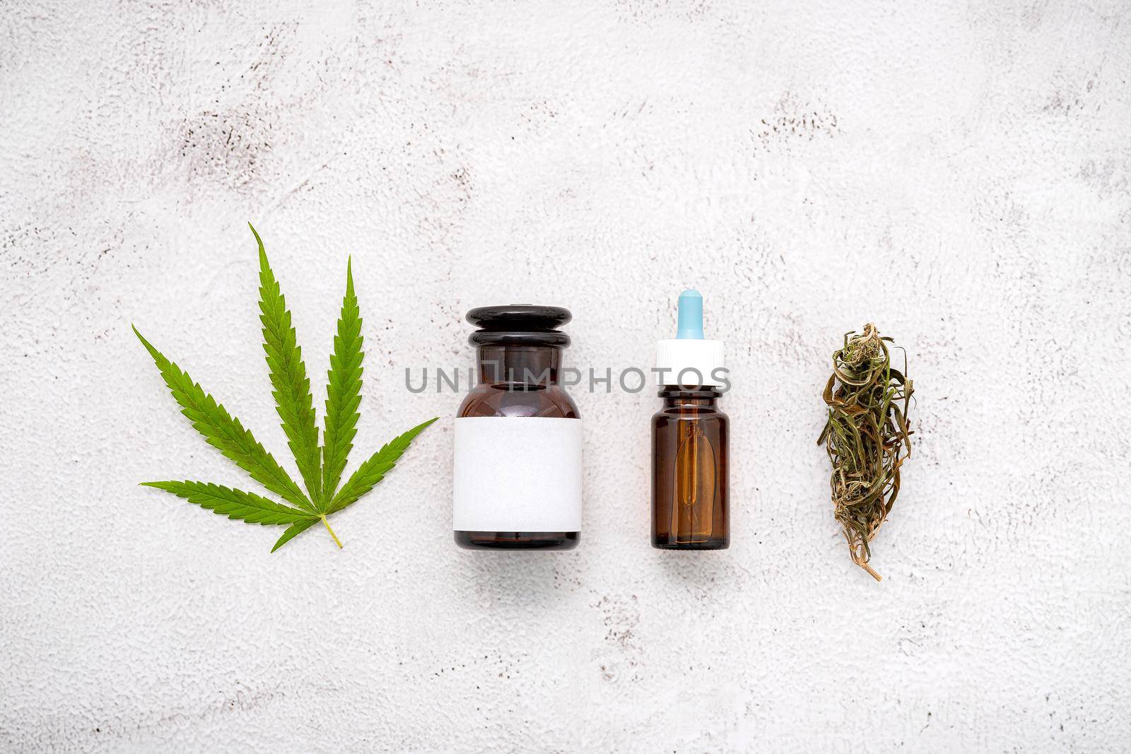 Glass bottle of cannabis oil with white mortar and hemp leaves set up  on concrete background.