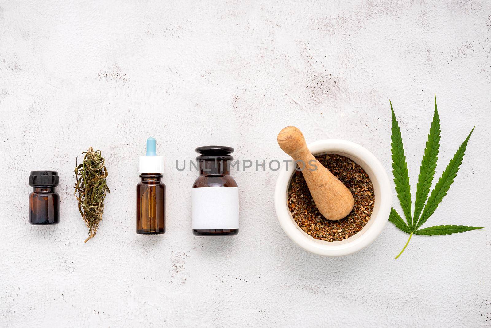 Glass bottle of cannabis oil with white mortar and hemp leaves set up  on concrete background.