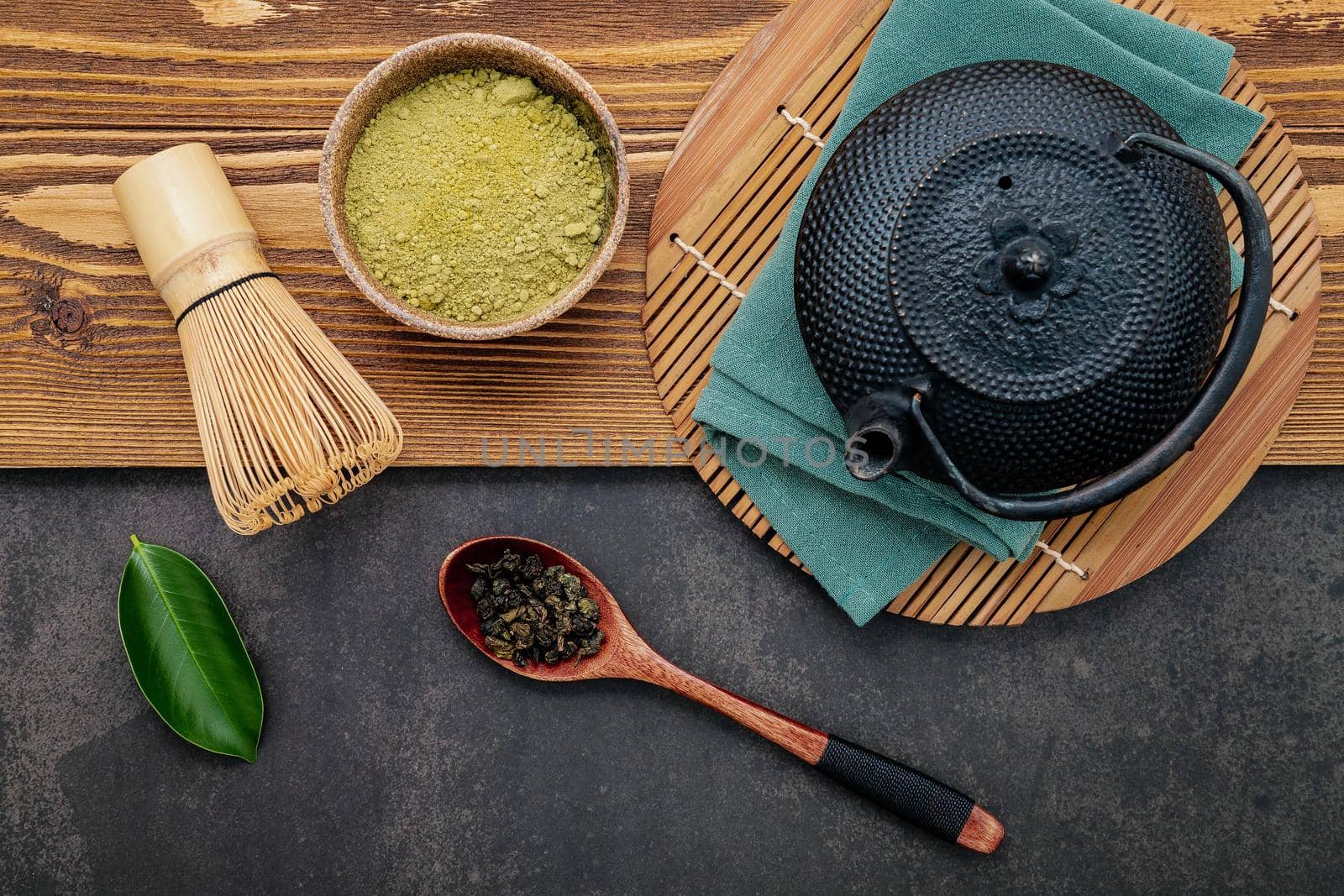 Black cast iron tea pot with herbal tea set up on dark stone background.