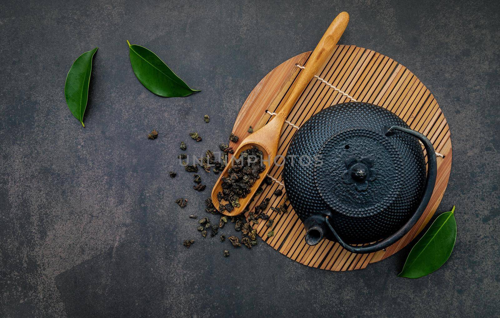  Black cast iron tea pot with herbal tea set up on dark stone background. by kerdkanno