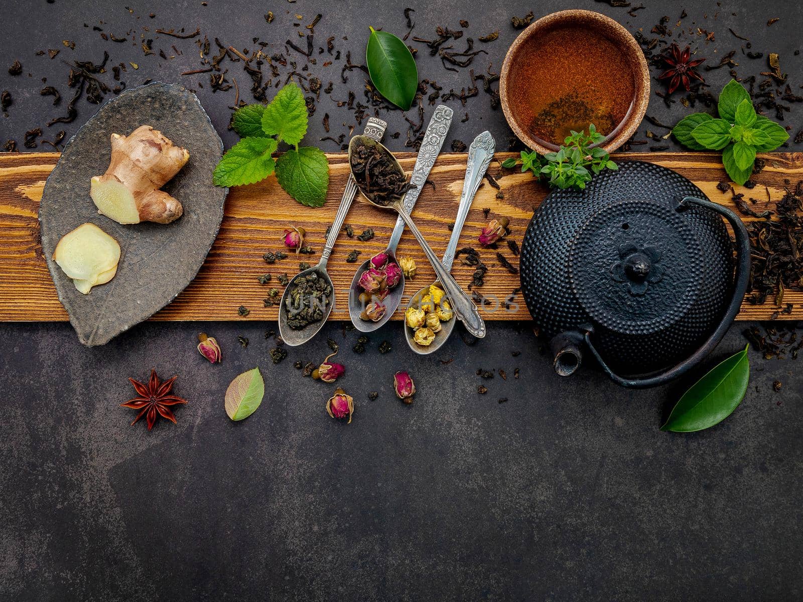 Black cast iron tea pot with herbal tea set up on dark stone background.