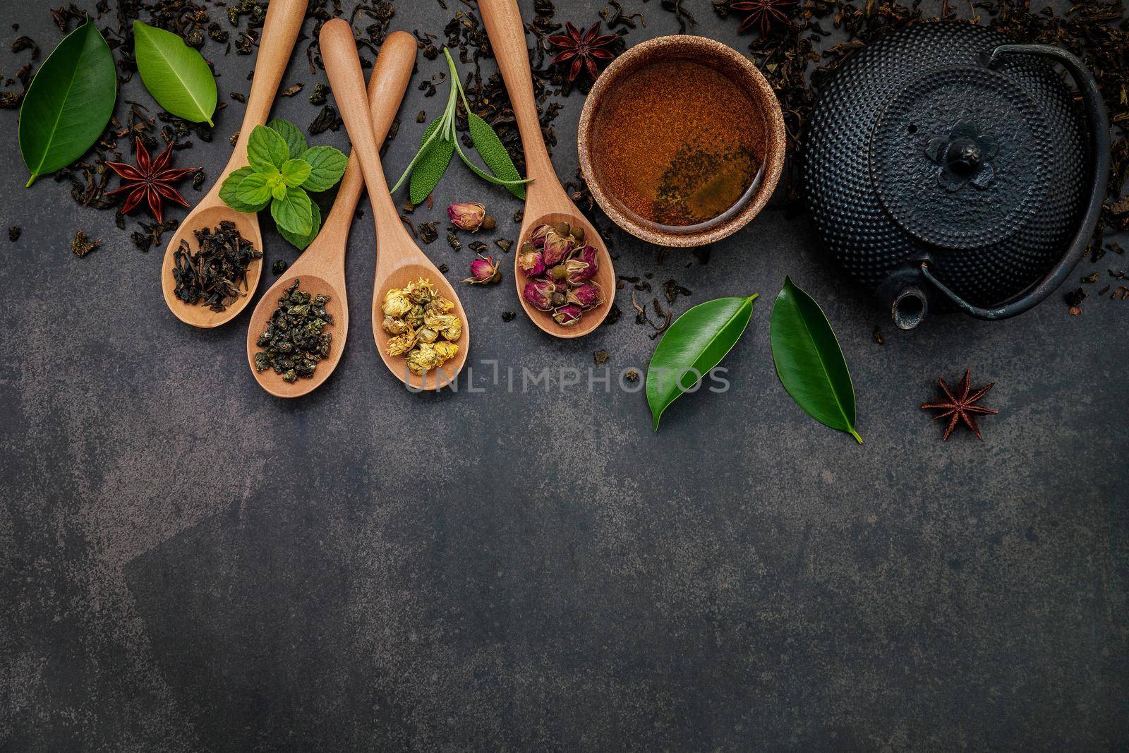 Black cast iron tea pot with herbal tea set up on dark stone background.