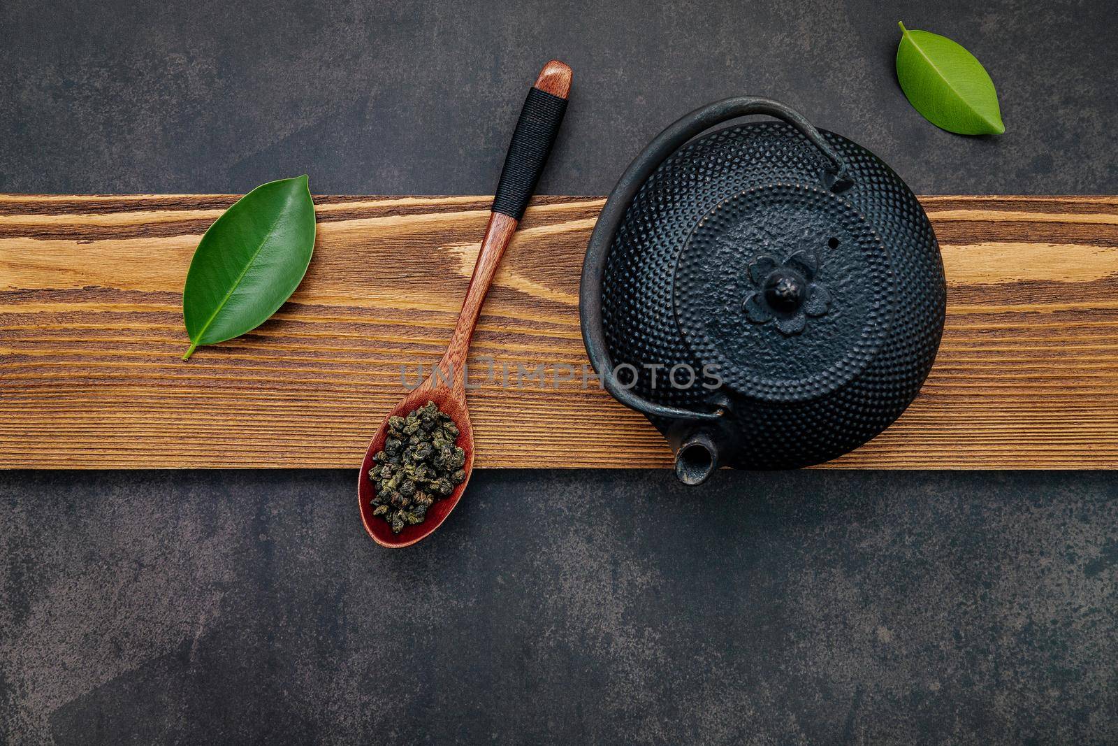 Black cast iron tea pot with herbal tea set up on dark stone background.