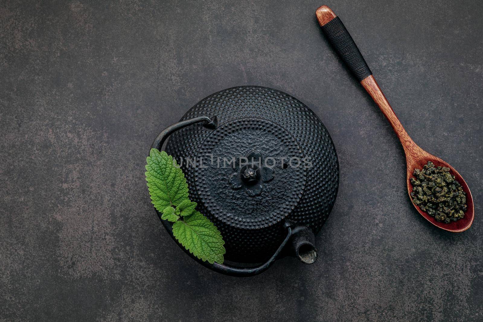 Black cast iron tea pot with herbal tea set up on dark stone background.